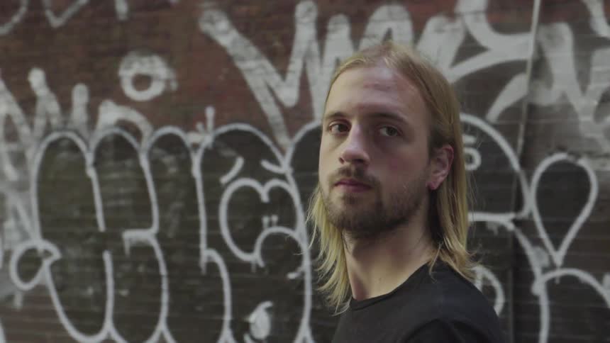 Bearded man walking alongside graffiti on a city street