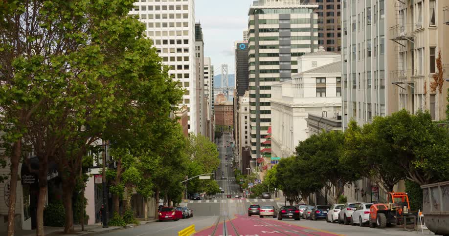 A city street with building cars driving and a person getting in to their car