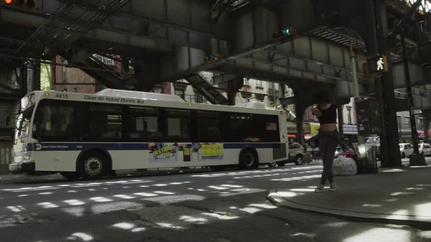 A woman dances on a sidewalk as a bus passes by