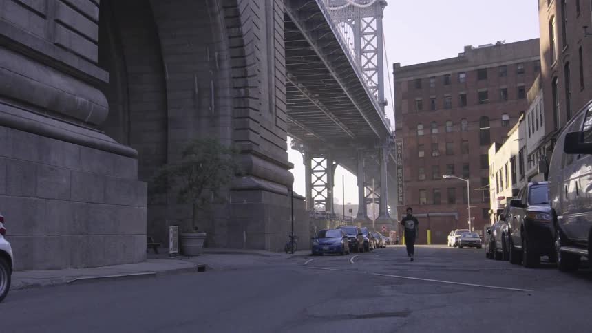 A man walks down a street next to many vehicles and a bridge