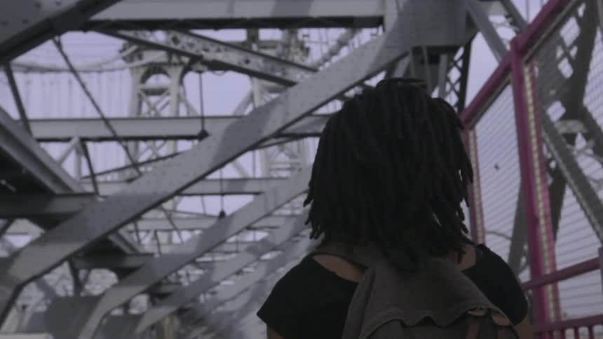 A woman in a black shirt walks under a bridge