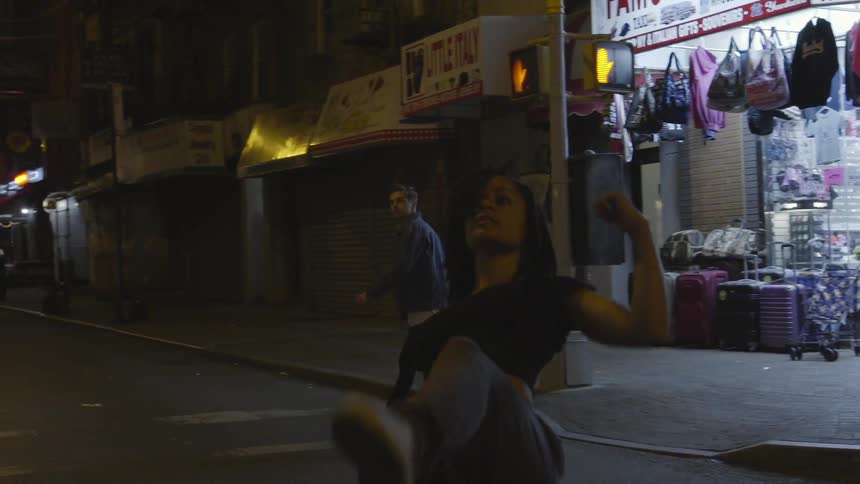 A woman in a black shirt dances slowly in the road