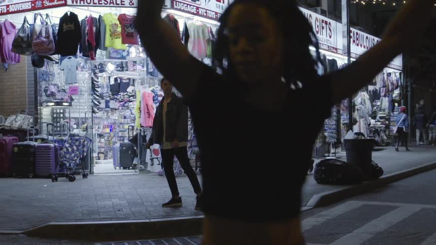 A man walks by a store at night while a woman dances in the street