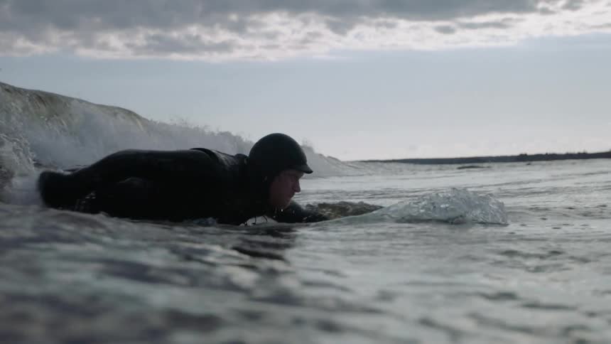 A man paddles his arms on a surfboard riding a wave