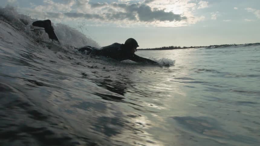A man paddles through the water in front of a wave