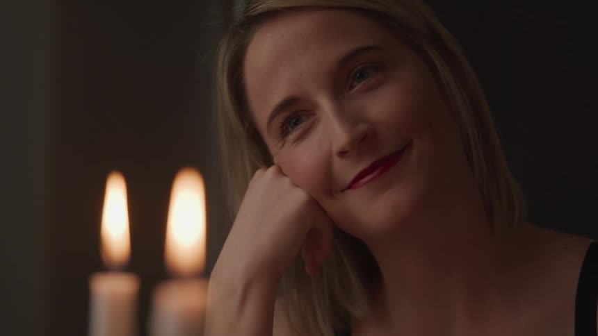 Woman smiles and looks at someone lovingly while sitting at the candle lit dinner table