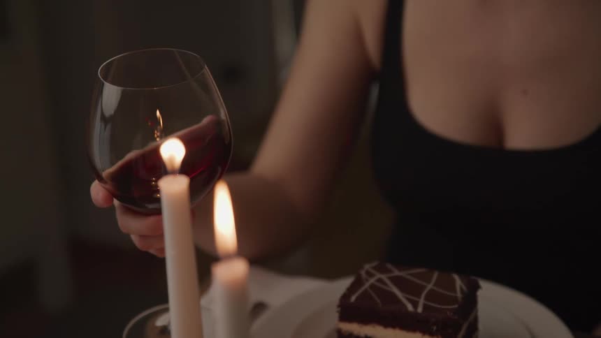 A woman swirls a glass of red wine while eating a candlelit dinner