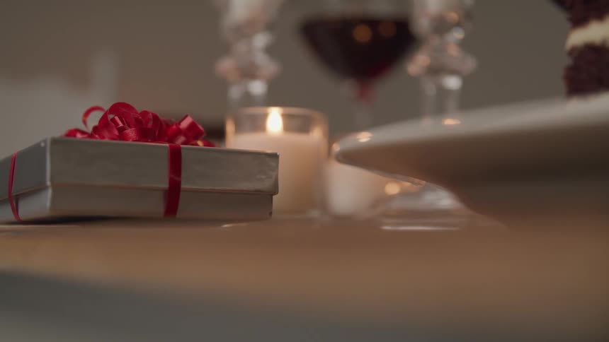 A gift sitting on a table with candles wine and dessert