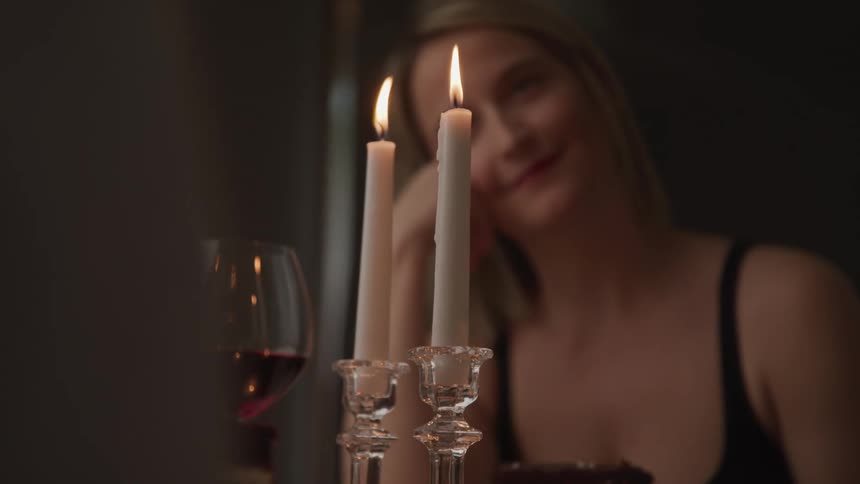 A young woman smiles as she sits at a table with candles dessert and red wine