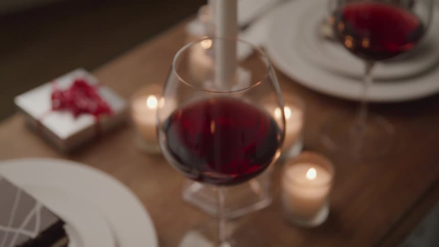 A wine glass on a wooden table covered in candles and dining ware