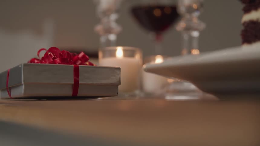 Small present wrapped in red ribbon on the surface of a table served for a candlelight dinner