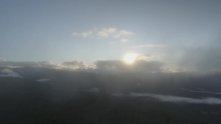 A countryside covered in forest seen through clouds blowing across the camera