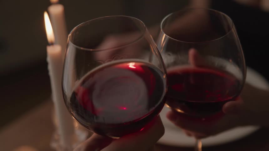 A man and woman toast one another with red wine