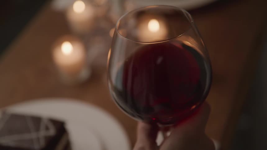 A person swirling a glass of red wine during a candlelit dinner