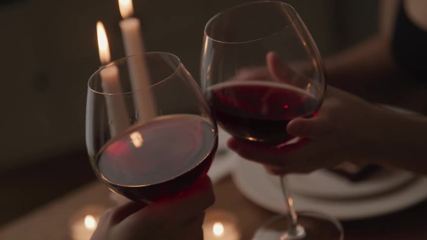 Woman and man sitting at a table with candles clinks wine glasses in a restaurant