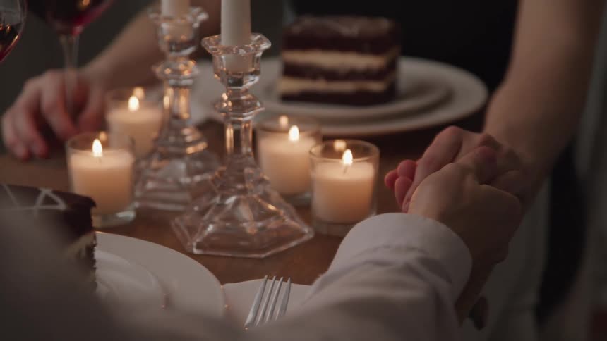 A man and woman hold hands at a table with dessert and wine