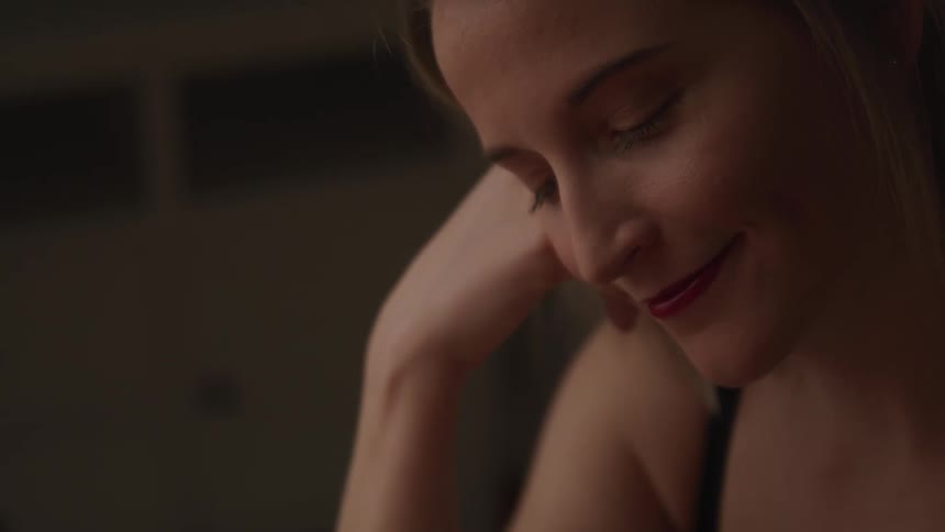 A woman putting her hand on her cheek while smiling and looking off into the distance with a door in the background