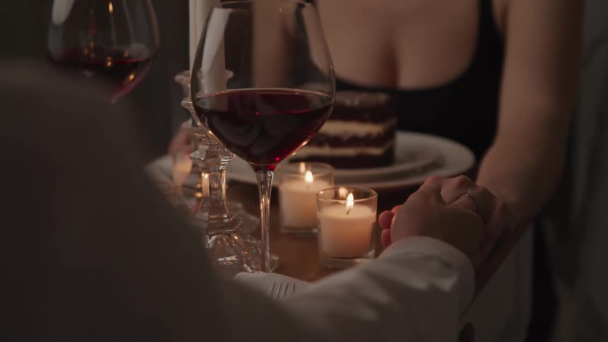 A couple sit across from each other at a small restaurant table as they enjoy wine and desert