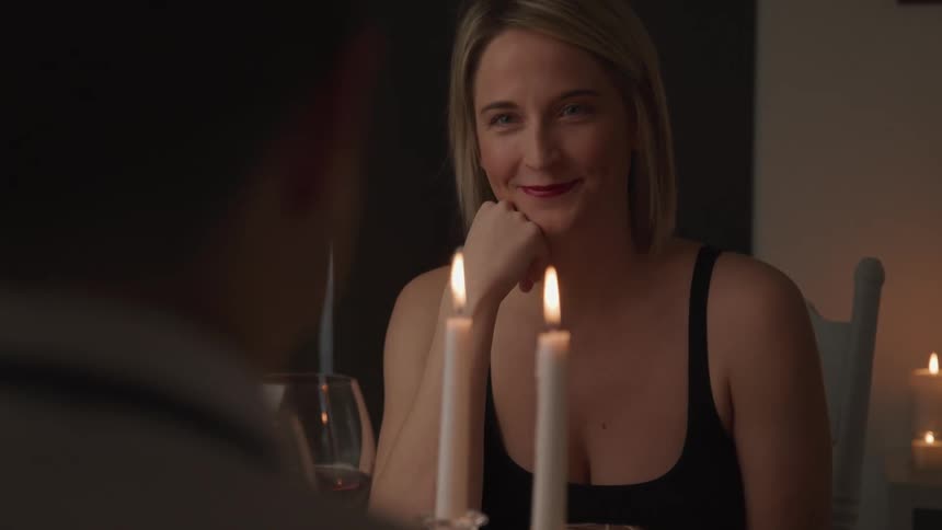 A woman smiles at a man sitting across from her at a dining table adorned with candles