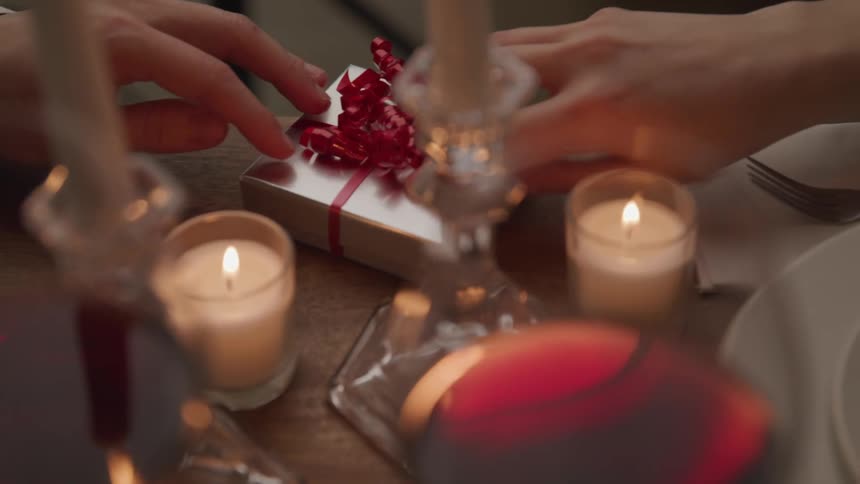 A man pushes a gift across a table and a woman accepts it and slides it towards herself