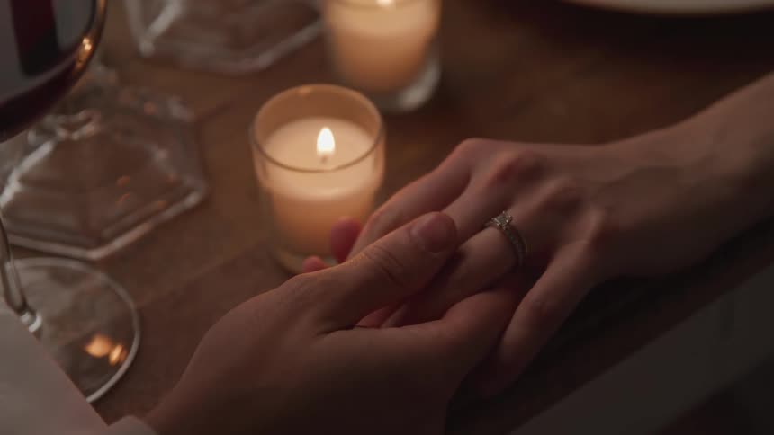 A man and woman hold hands at a candlelit dinner table