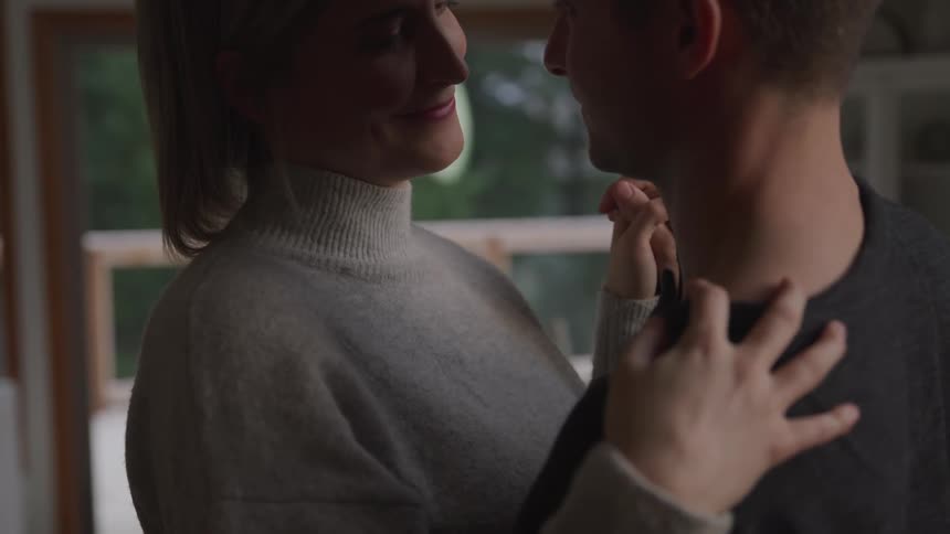Blonde woman with a grey turtleneck sweater and man with a black sweater dance together