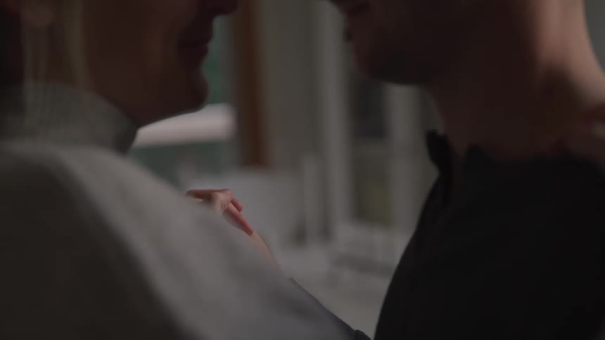 Male and female couple slow dance together at home as they smile and gaze into one anothers eyes