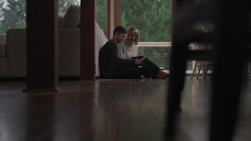 A man and woman sit on the floor with wine glasses