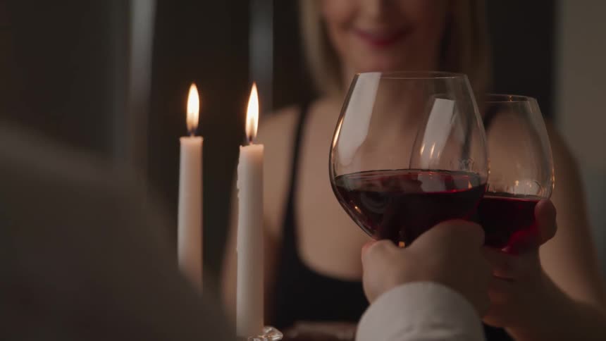 A man and woman clink their wine glasses together while sitting at a candlelit table