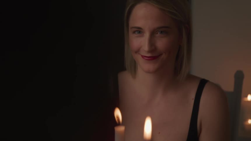 A couple sitting at a candle lit table as the woman receives a small gift box