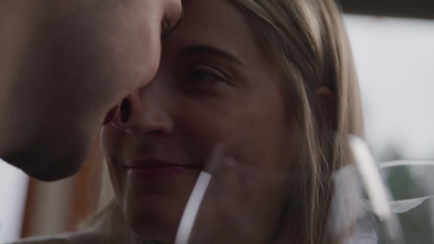 A man and woman with their heads together look into one anothers eyes over glasses of wine