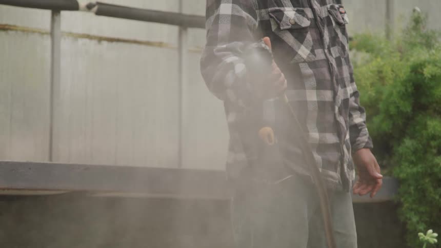 A man in a flannel shirt waters his lawn