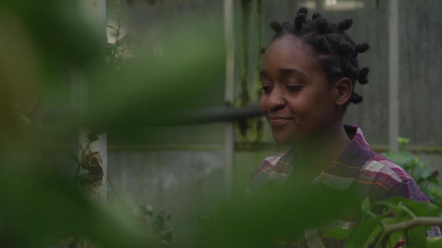 A woman smiles while standing near some plants