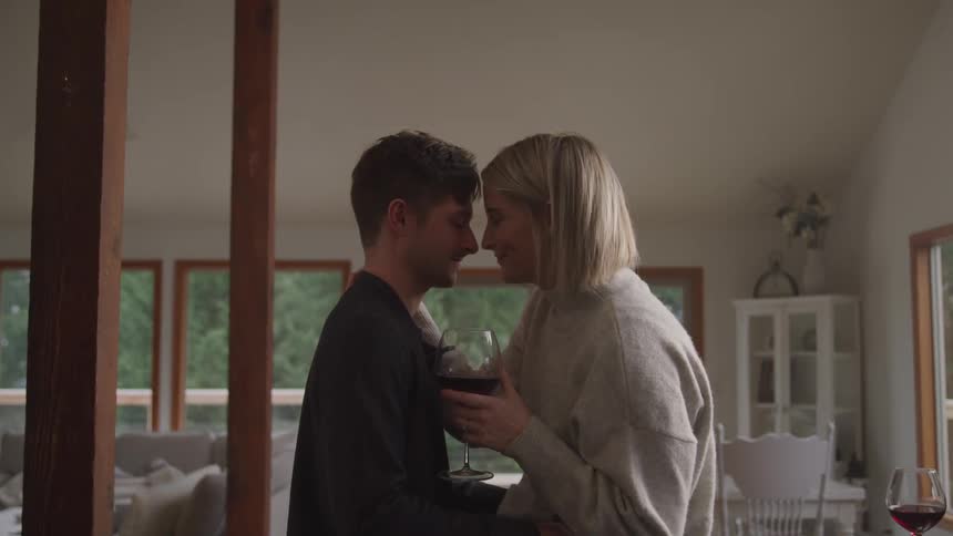A woman holds a wine glass and leans in to her husbands forehead romantically