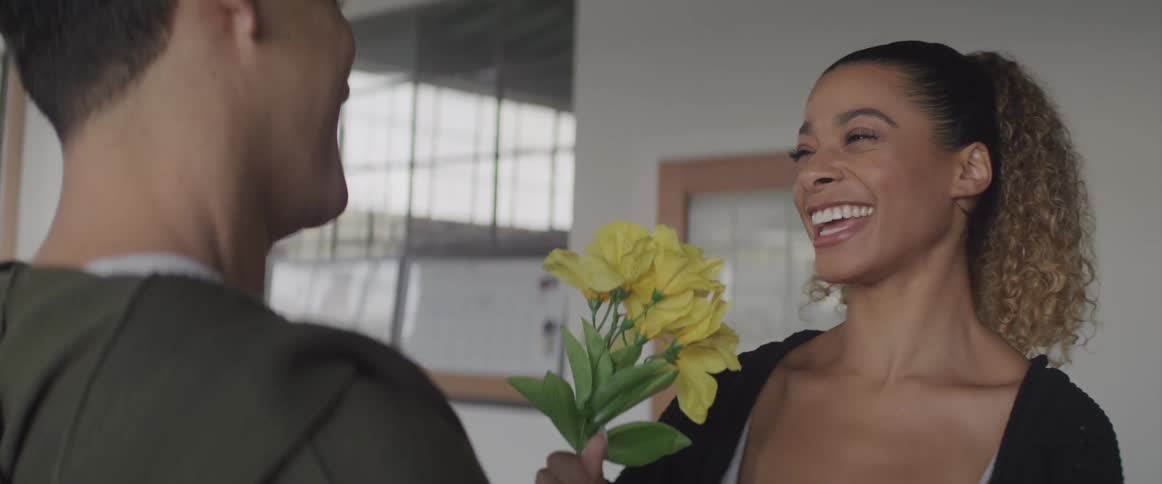 A woman holds a small bouquet of flowers and hugs the man standing in front of her