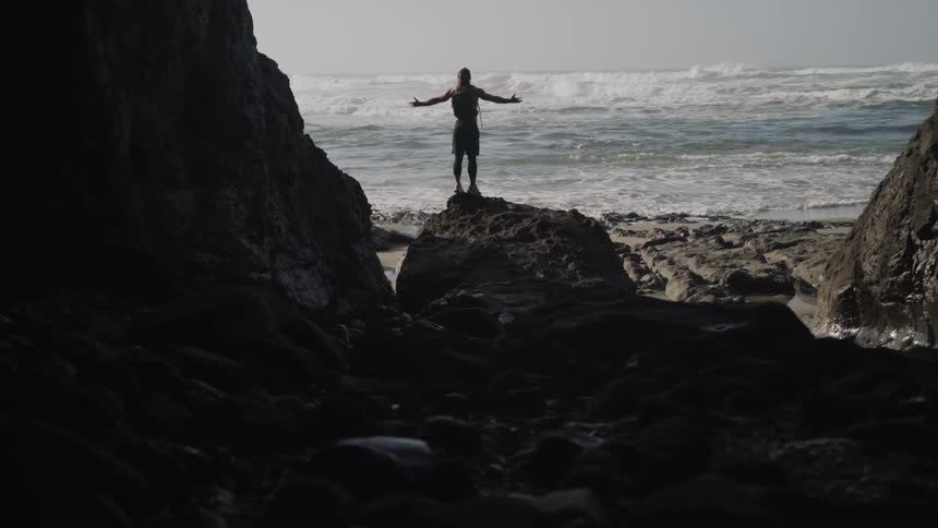A man is standing on a rock by the beach