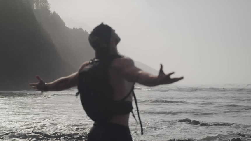 A man stands on the ocean edge and raises his arms up away from his side