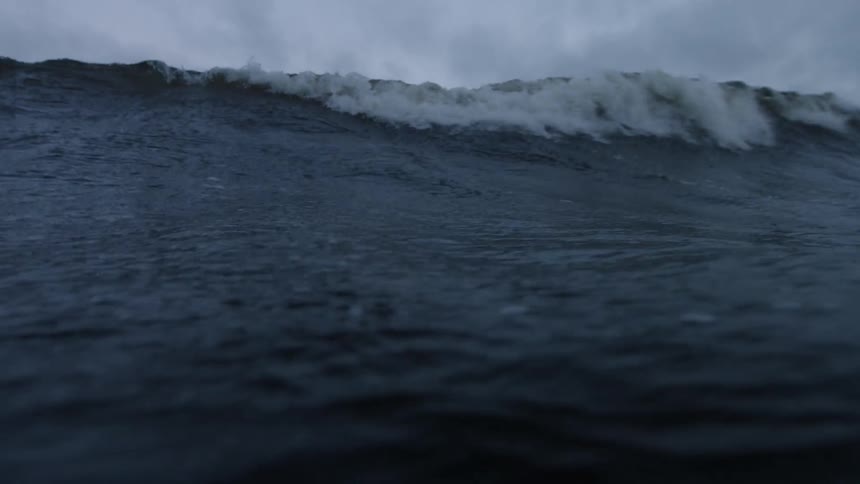 A large waves crashes on a cloudy day