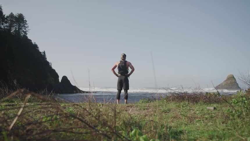 A man stands on the shore and looks out at the water