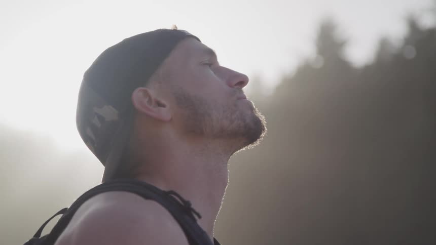 A man with a hat and a backpack looking towards the sky with trees in the background