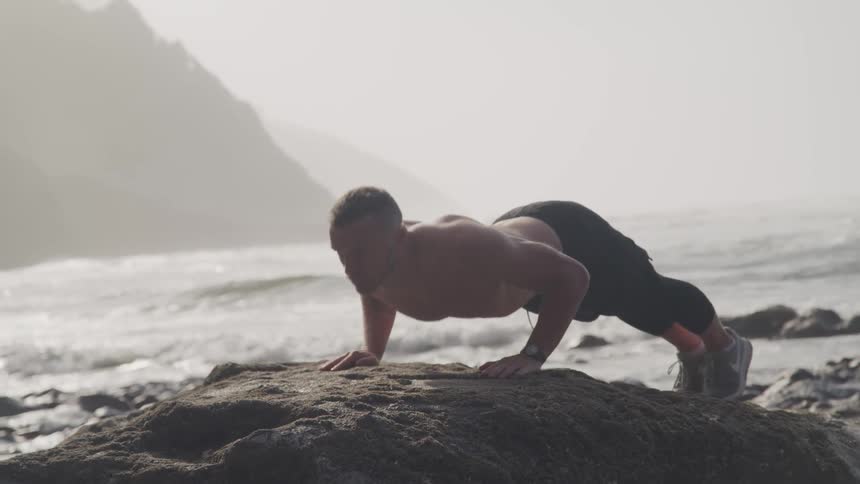 A man does push ups on a beach side rock