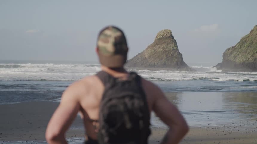 A man is standing by the coast of a beach