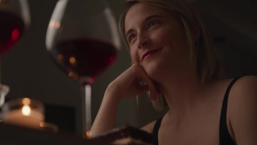 A woman looks up and smiles at her date as they sit in a bar with glasses of red wine