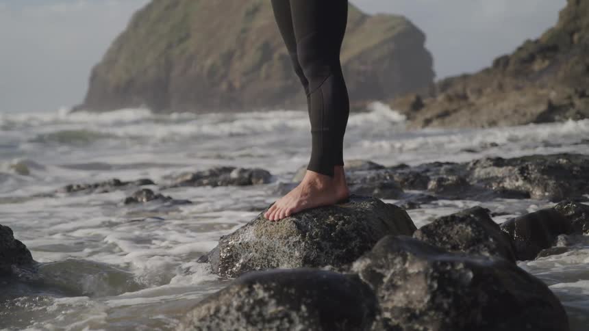 A person standing on a rock on the beach with the sky in the background
