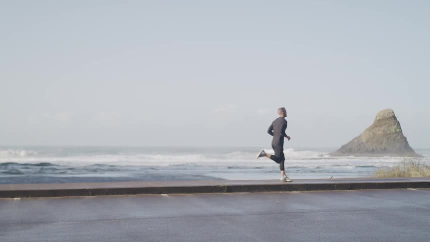 A man runs on the walkway between a parking lot and the ocean