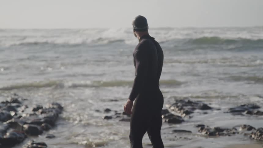 A male wearing a wet suit standing on a beach