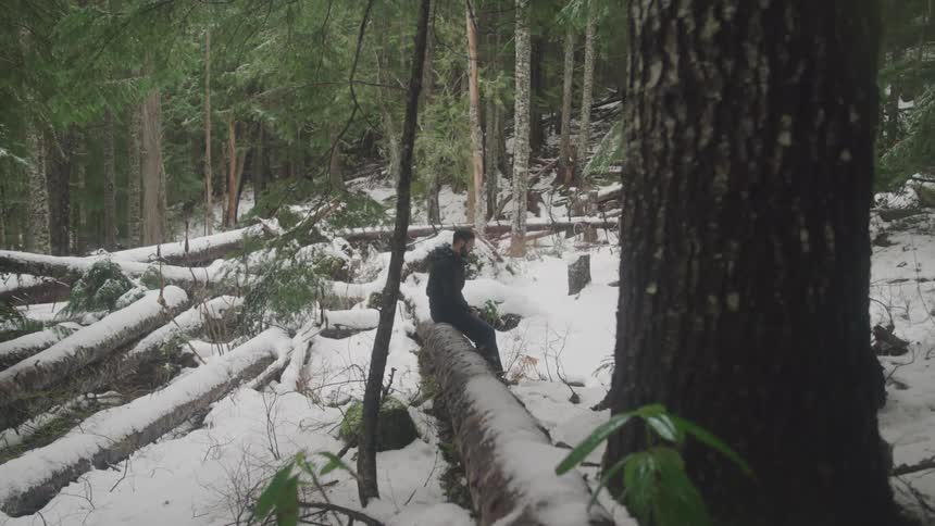 A man sitting on a log in the forest covered in snow