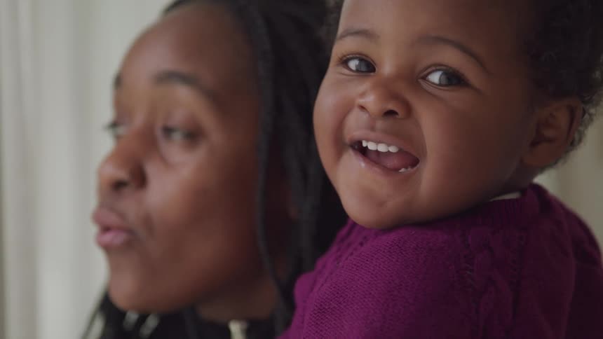 A woman holds a smiling toddler who is wearing a purple sweater