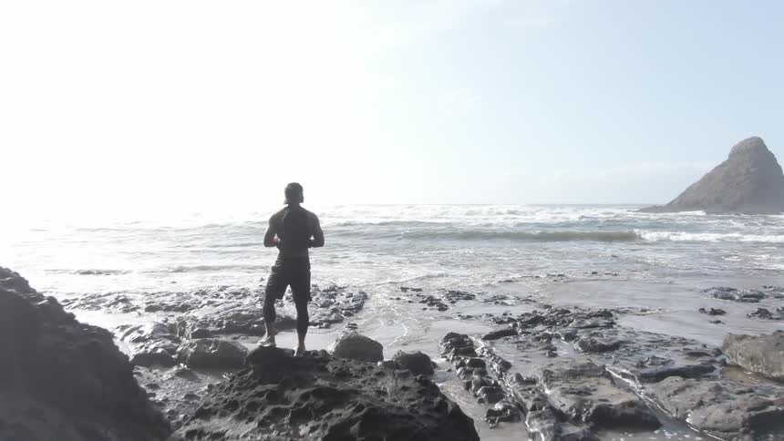 A man is standing on the rocks by the shore