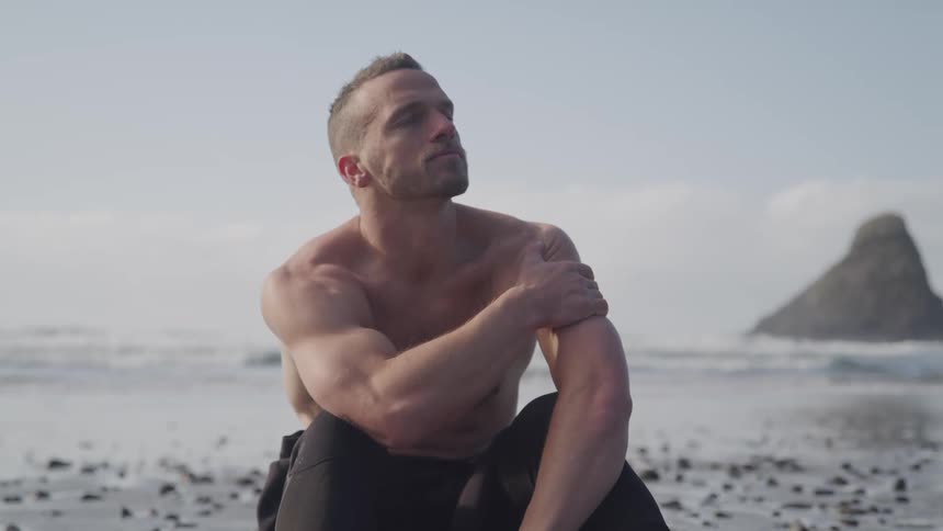 Shirtless muscular man sitting on the sand of a beach
